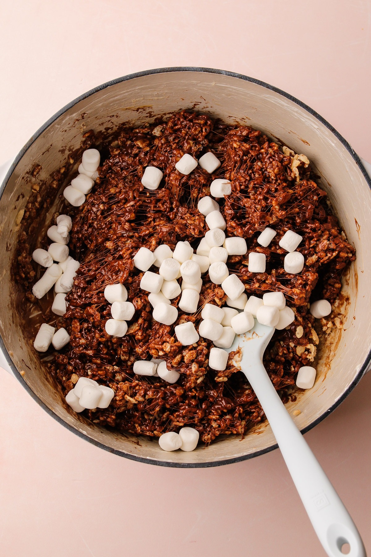 Pressing the chocolate rice crispy treats mixture into a baking pan with extra marshmallows on top.