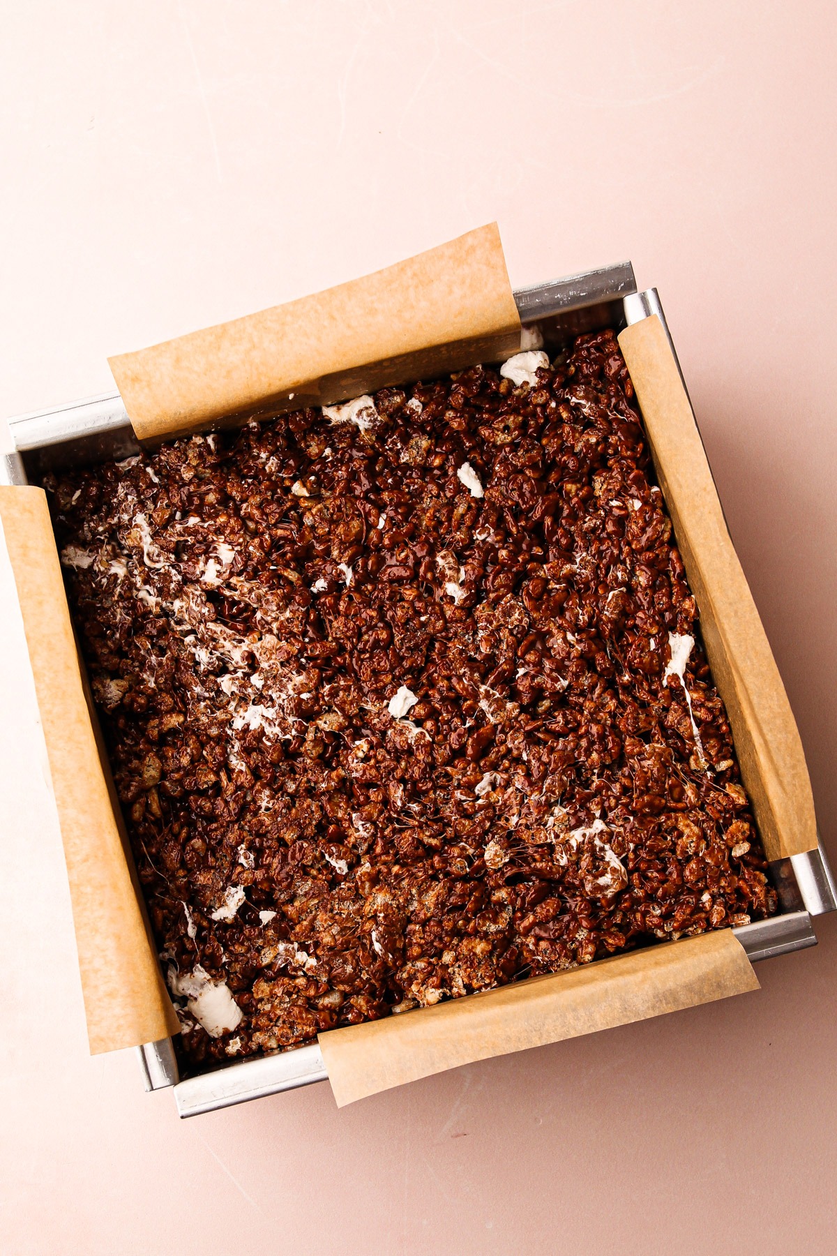 Chocolate rice crispy treats mixture pressed into a parchment-lined baking pan.