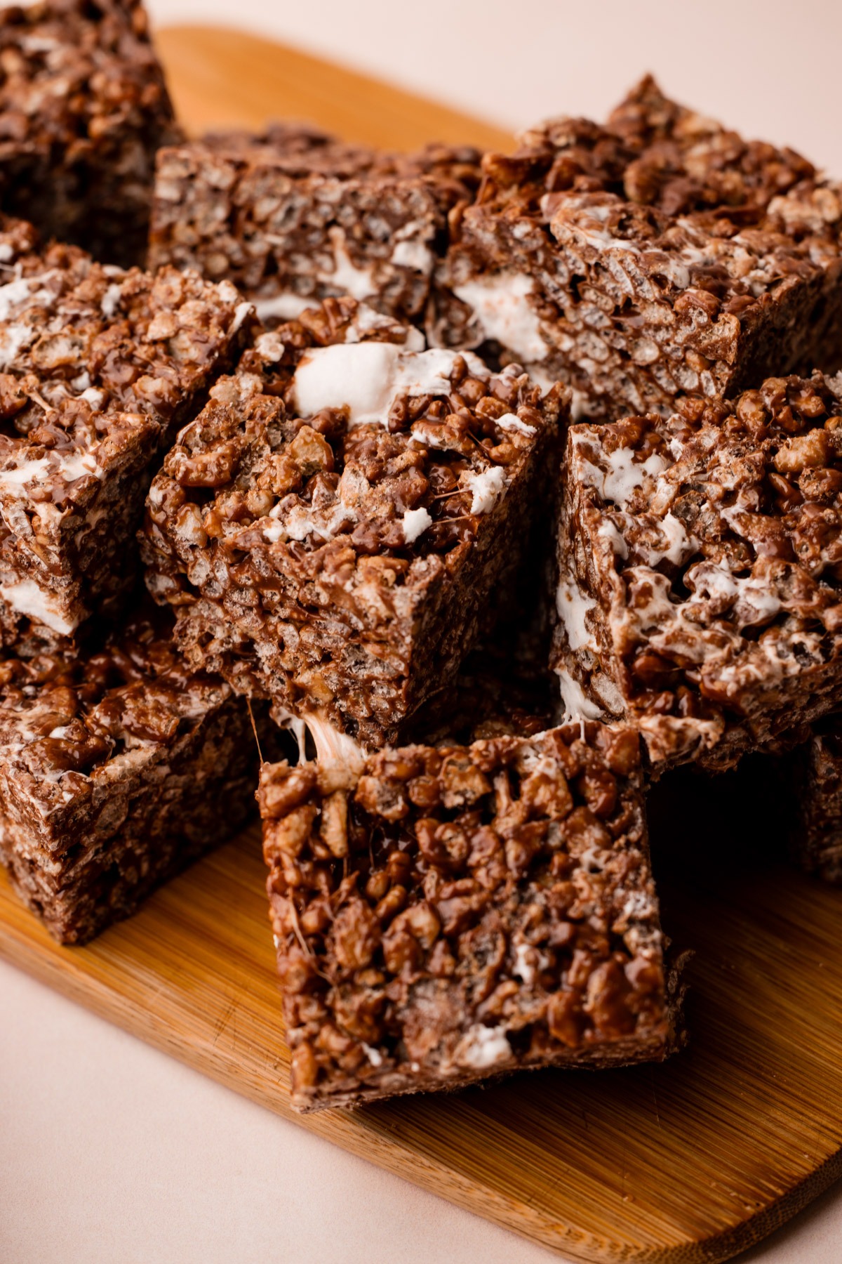 Sliced chocolate rice crispy treats stacked on a wooden board.