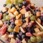 Fruit salad with condensed milk served in a glass bowl with a gold spoon.