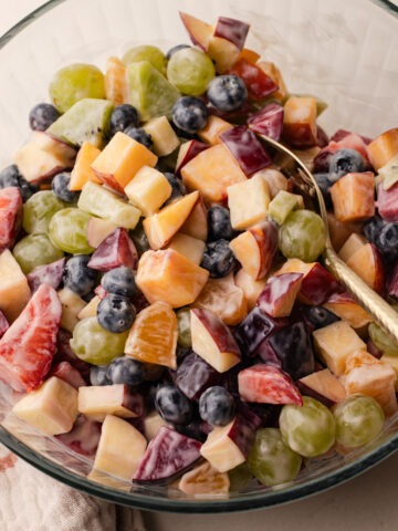 Fruit salad with condensed milk served in a glass bowl with a gold spoon.