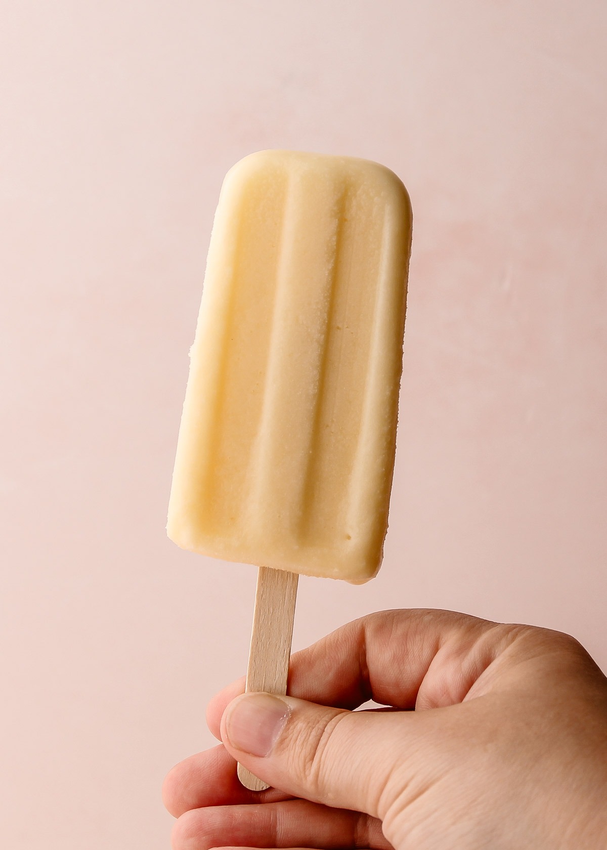 A hand holding a pineapple coconut popsicle.