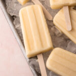 A tray full of ice with coconut pineapple popsicles laying on top.