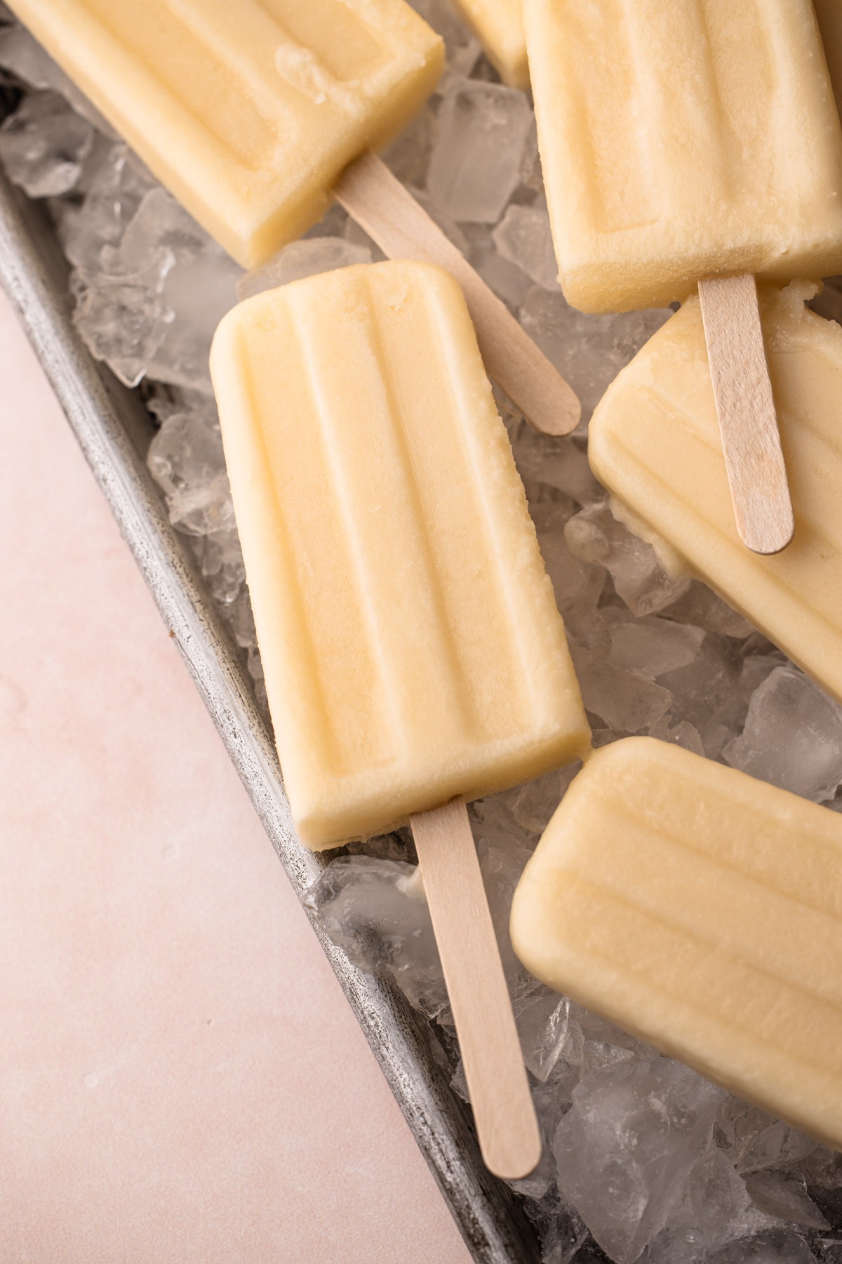 A tray full of ice with coconut pineapple popsicles laying on top.