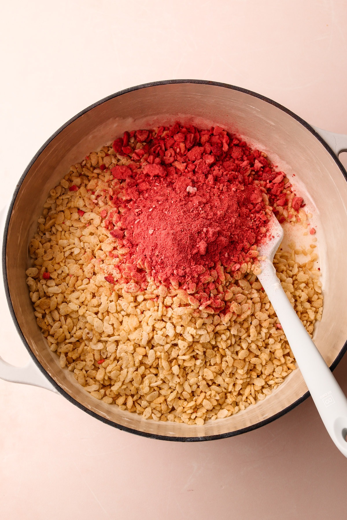 Mixing freeze-dried strawberries with rice crispy cereal in a pot.