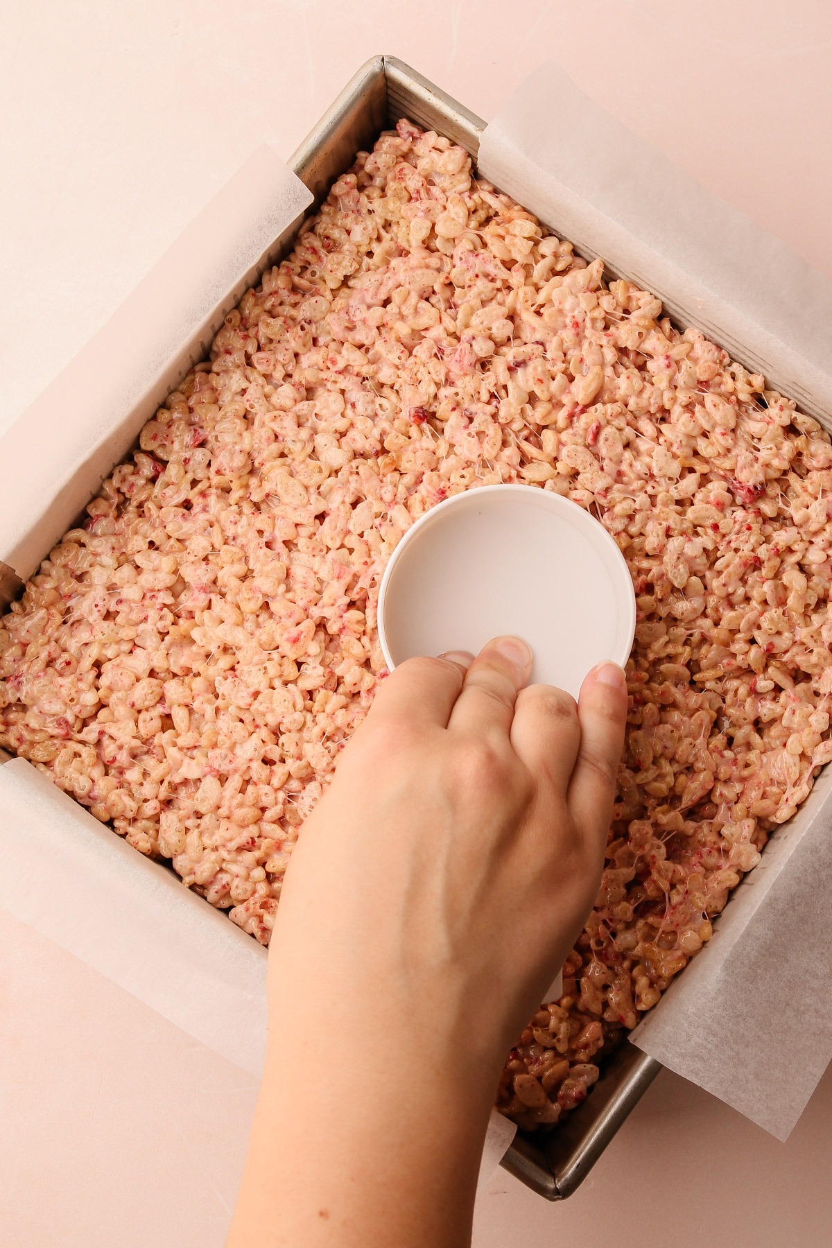 Pressing down the strawberry rice crispy treats mixture in a pan.