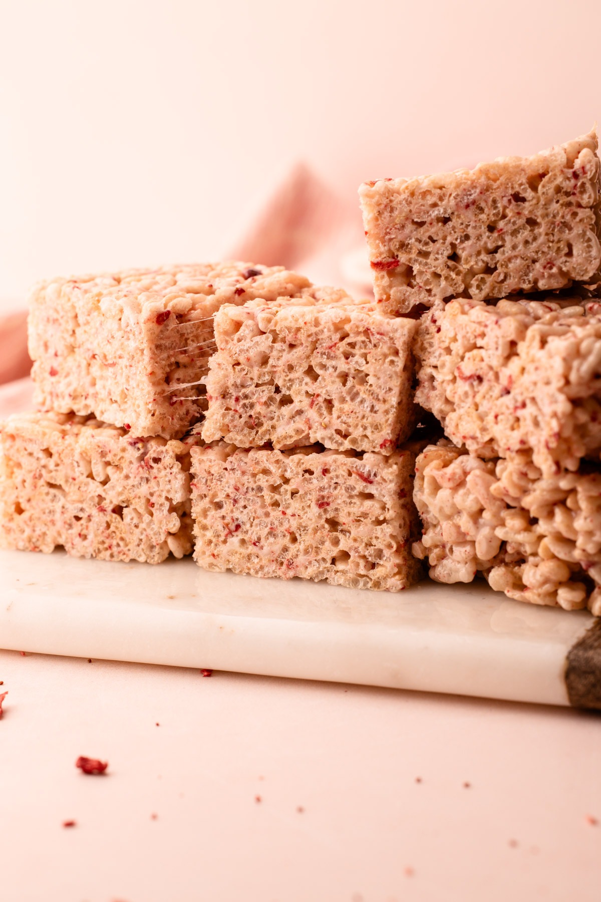 Stacked pieces of strawberry rice crispy treats on a marble slab.