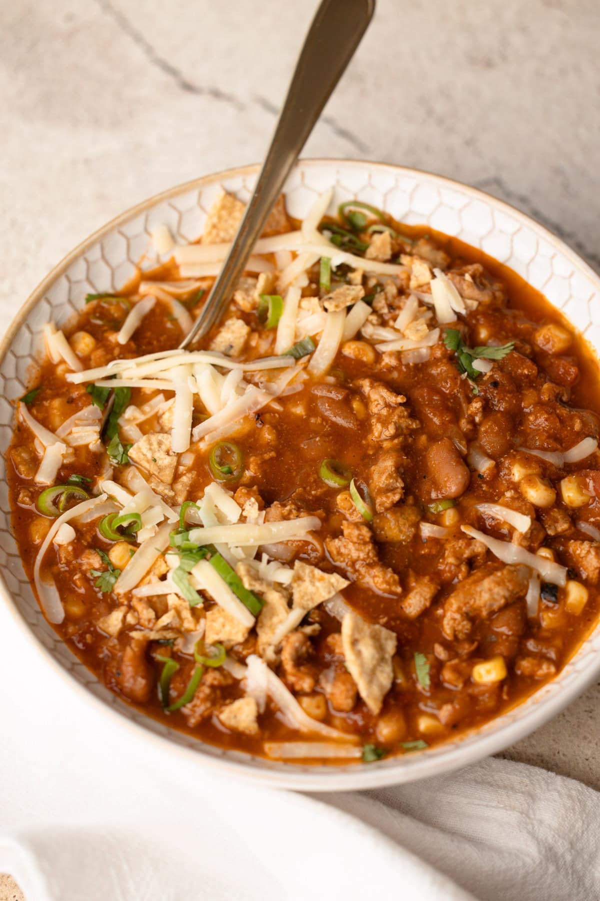 Hearty bowl of easy turkey chili topped with shredded cheese, green onions, and crushed tortilla chips.