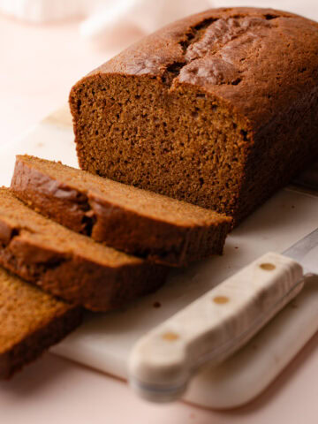 Sliced pumpkin bread made with whole wheat, arranged on a marble cutting board with a knife nearby.