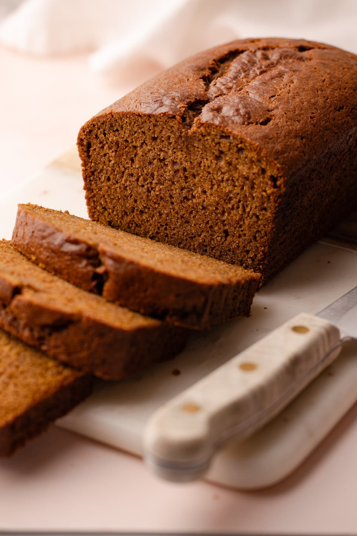 Sliced pumpkin bread made with whole wheat, arranged on a marble cutting board with a knife nearby.