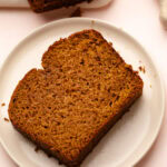 A thick slice of pumpkin bread whole wheat resting on a white plate, showcasing the dense crumb.