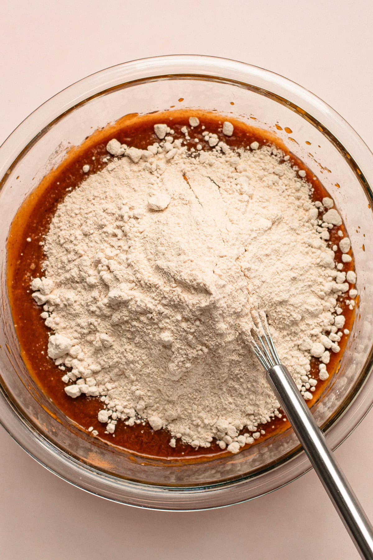 Whole wheat flour added to pumpkin bread batter in a clear bowl with a whisk.