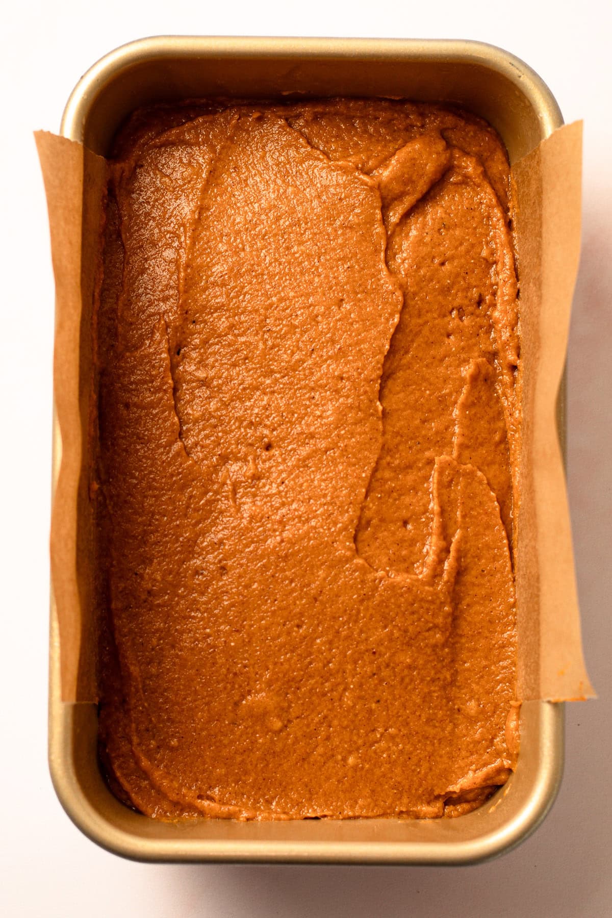 Unbaked whole wheat pumpkin bread batter spread evenly in a parchment-lined loaf pan.