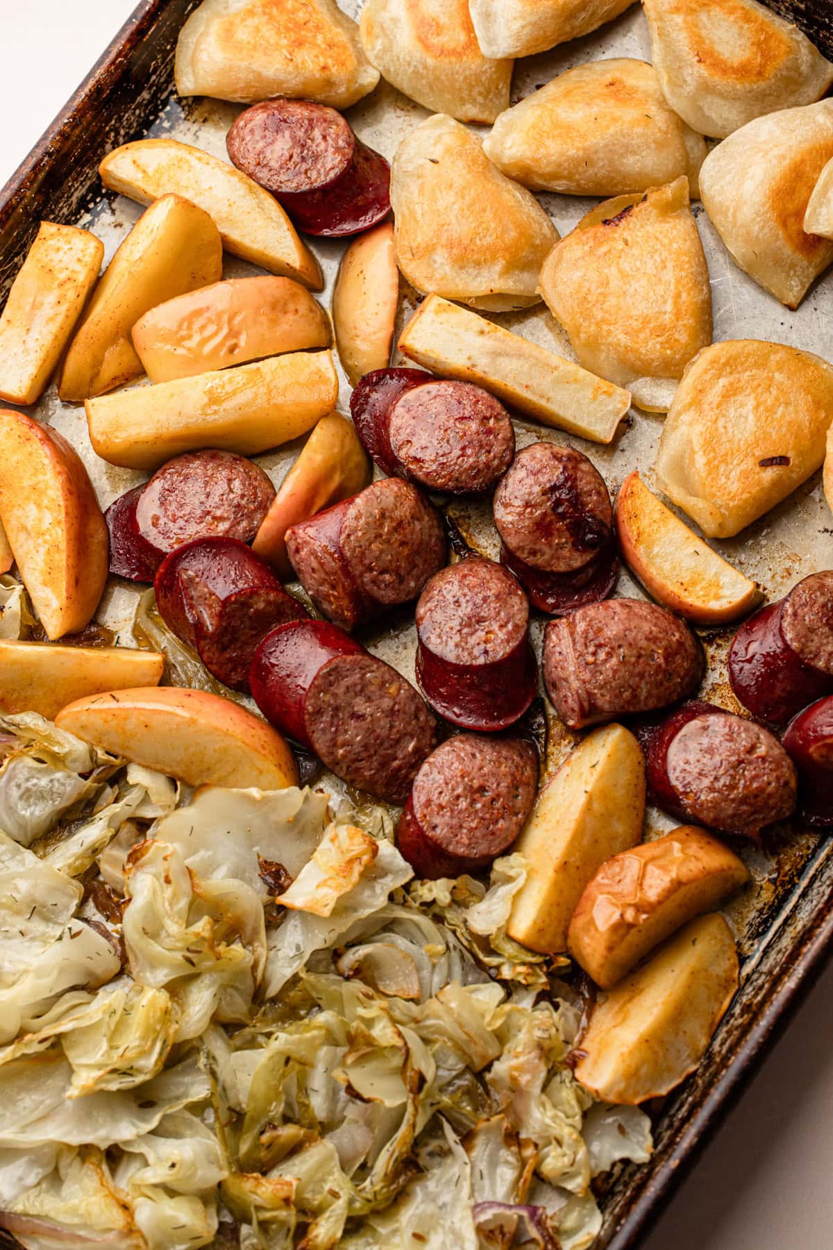 Golden pierogis, seared kielbasa, and roasted apples on a sheet pan, showcasing a savory and sweet pierogi and kielbasa recipe.