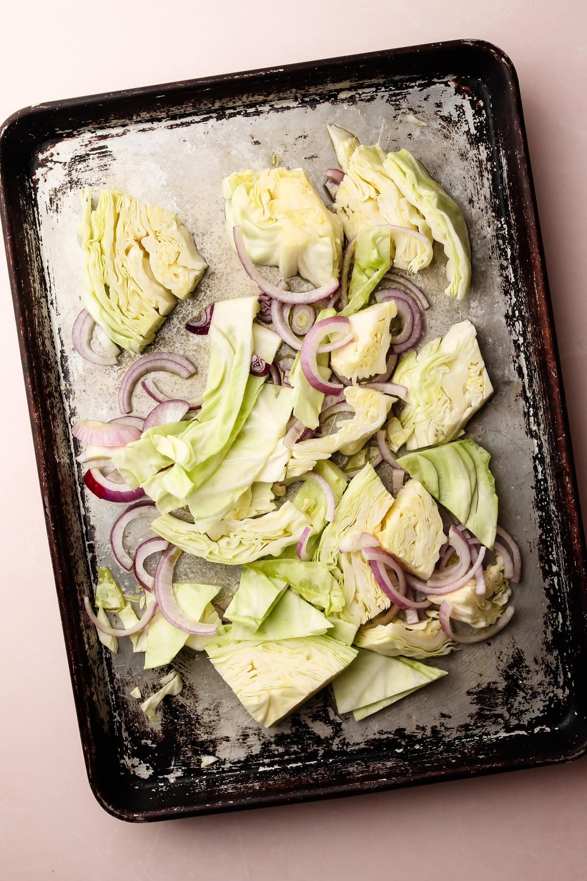 Raw cabbage wedges and sliced red onions arranged on a baking sheet, ready for roasting.