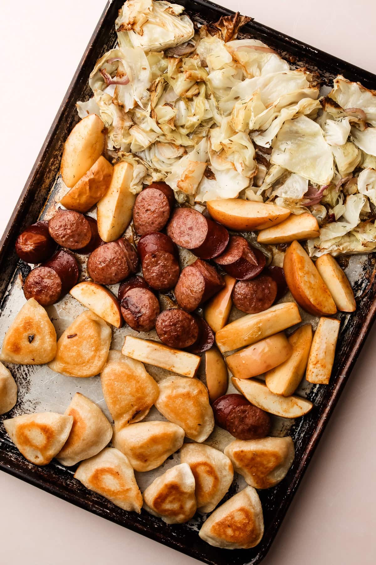 Roasted pierogis, caramelized apples, and savory kielbasa nestled among roasted cabbage, a complete sheetpan meal.