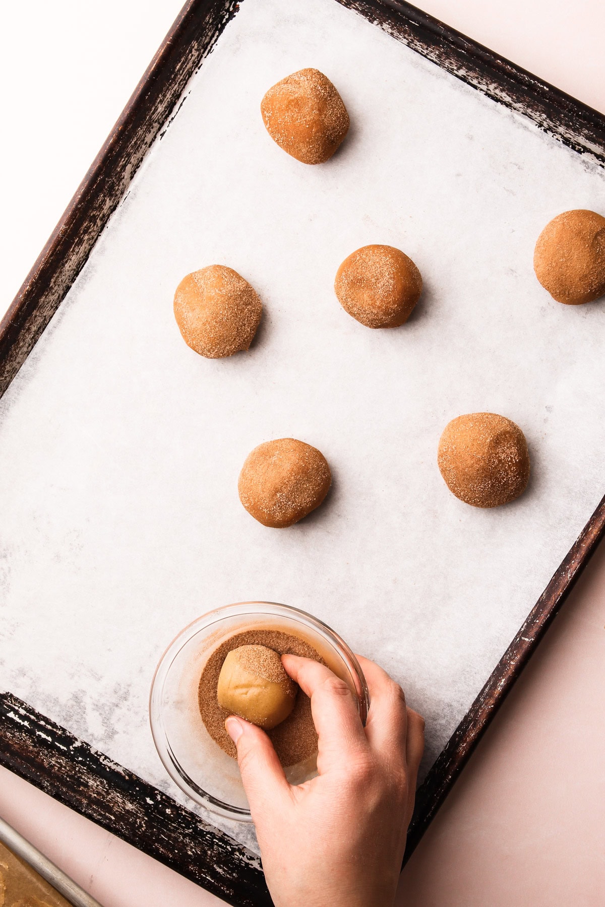 A hand dipping snickerdoodle dough into cinnamon sugar.