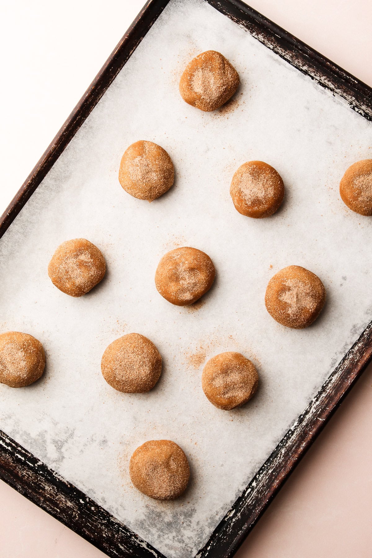 Flattened snickerdoodle dough balls coated in cinnamon sugar on a baking sheet.