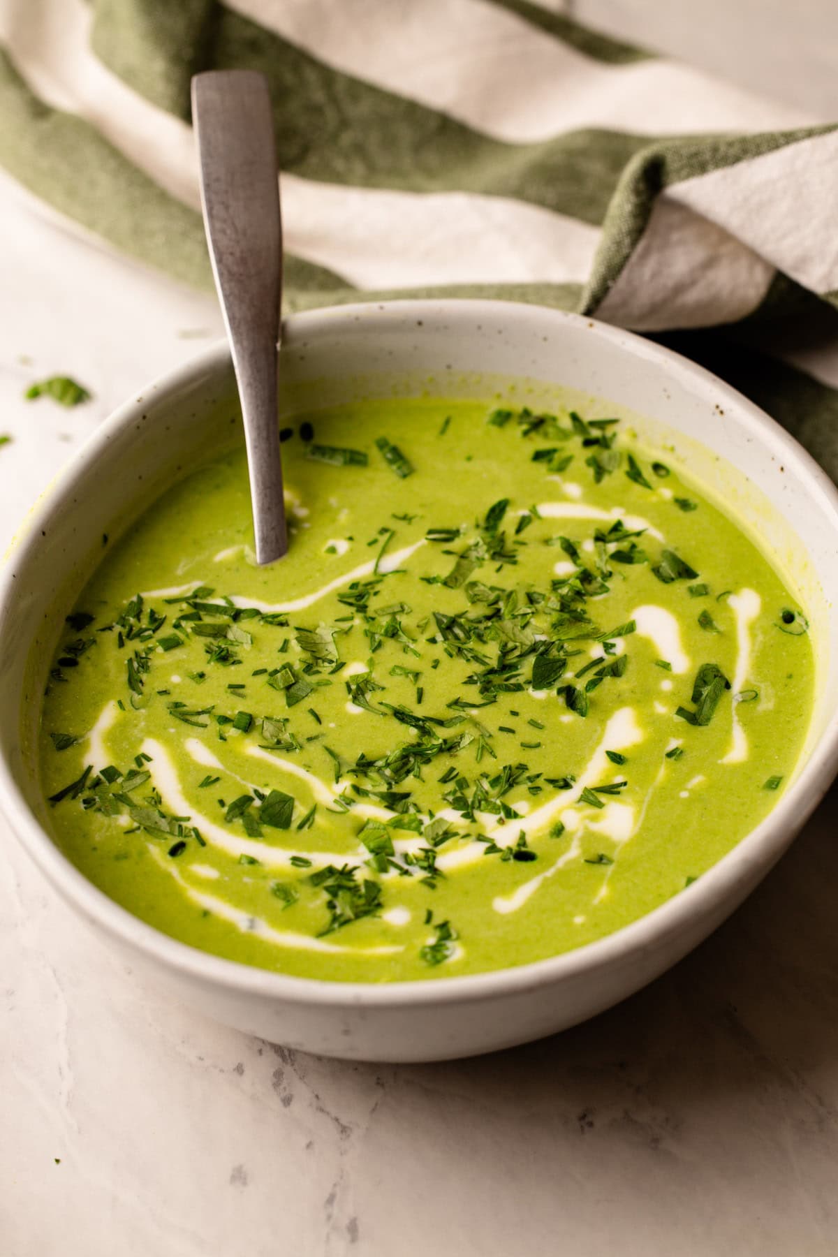 A bowl of green goddess soup with swirls of creme fraiche and herbs.