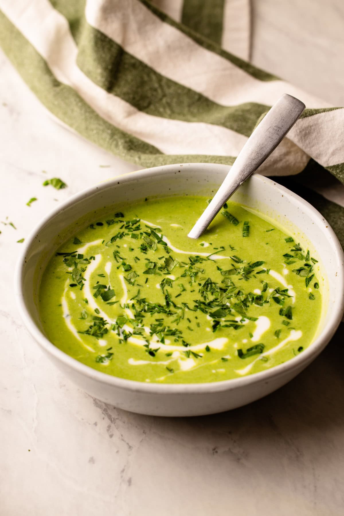 A bowl of green goddess soup with swirls of creme fraiche and herbs.