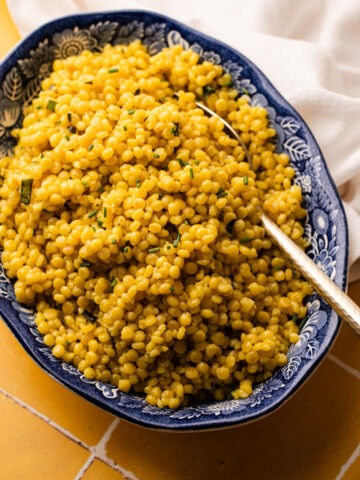 A large serving bowl filled with garlic and herb pearled couscous.