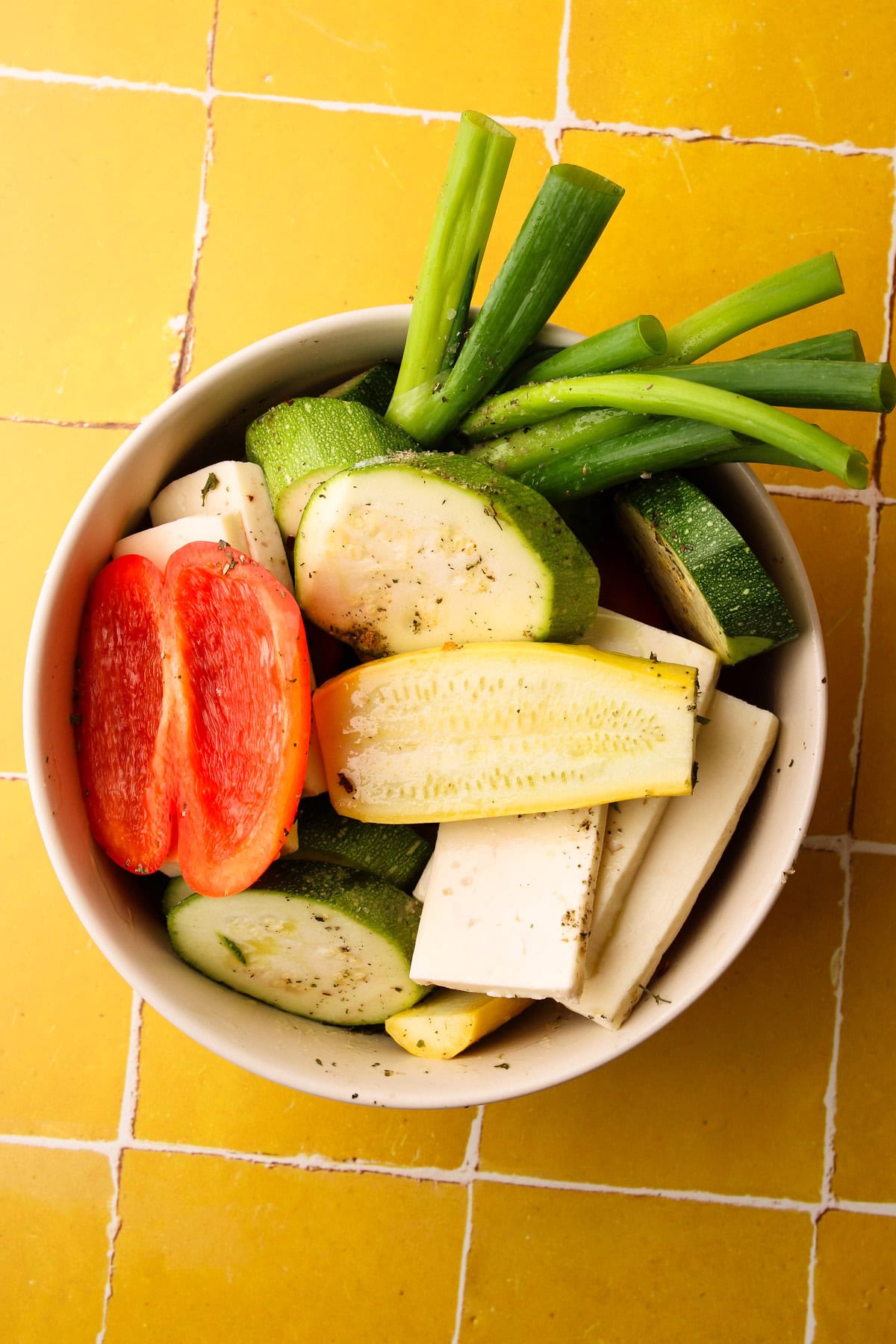 Raw cut veggies and halloumi cheese in a bowl with a marinade.