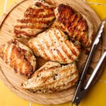Perfectly cooked grilled chicken breasts resting on a wood cutting board before being sliced.