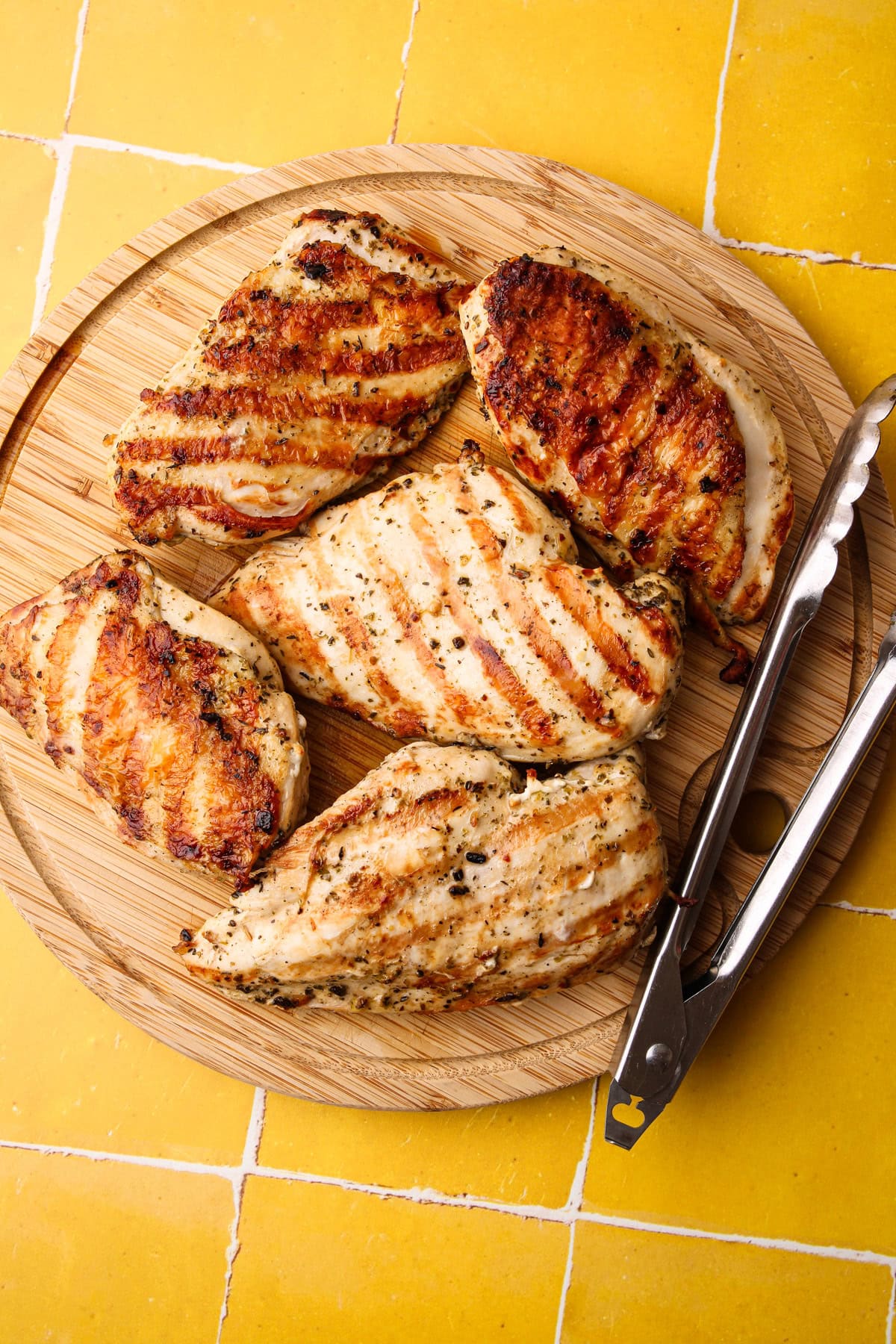 Perfectly cooked grilled chicken breasts resting on a wood cutting board before being sliced.