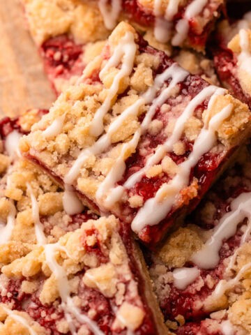 Baked and sliced strawberry crumble bars with a drizzle of icing stacked up on top of one another on a wood board.