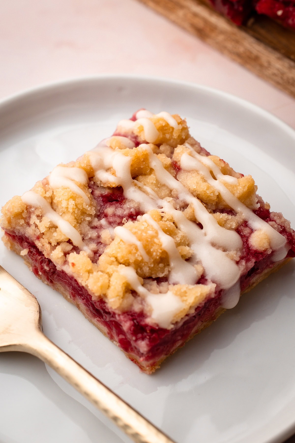 A slice of a strawberry crumble bars with a drizzle of on a plate.