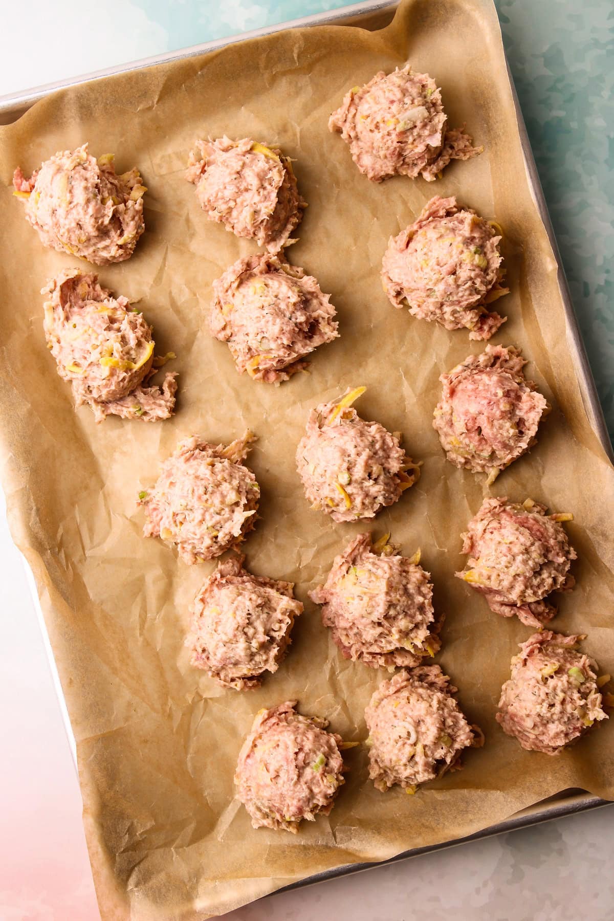 Unbaked scooped turkey zuccini meatball mix on a baking sheet.