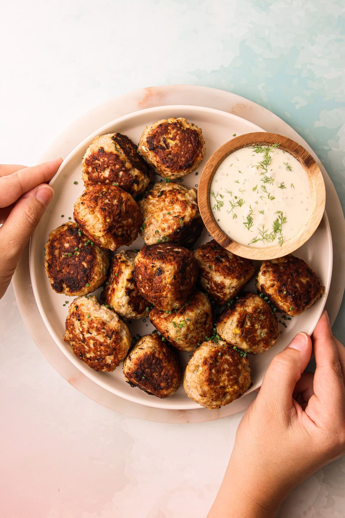 Two hands holding a serving platter of turkey zucchini meatballs.