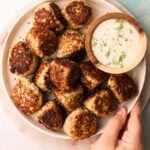 A hand holding a serving platter of turkey zucchini meatballs.