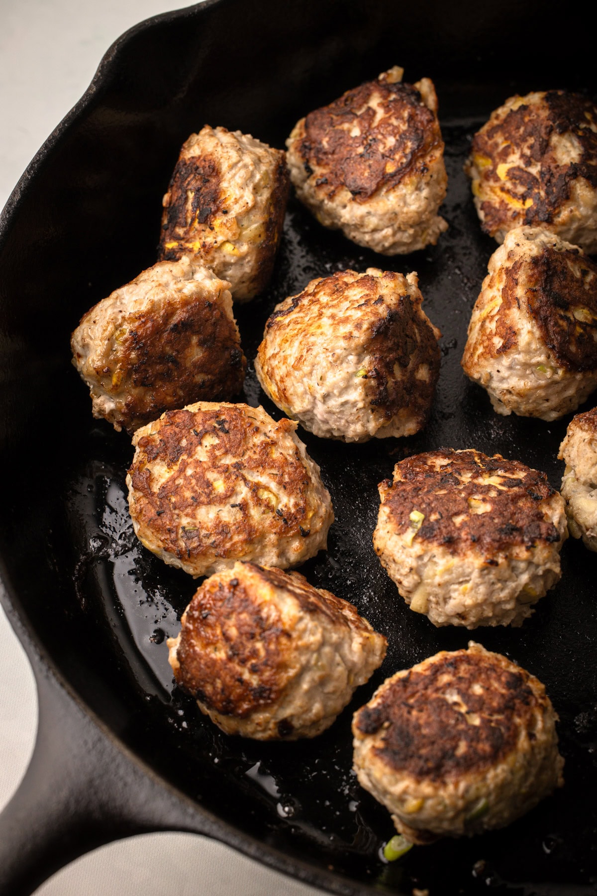 Meatballs made with turkey and zucchini cooking in a cast iron skillet.