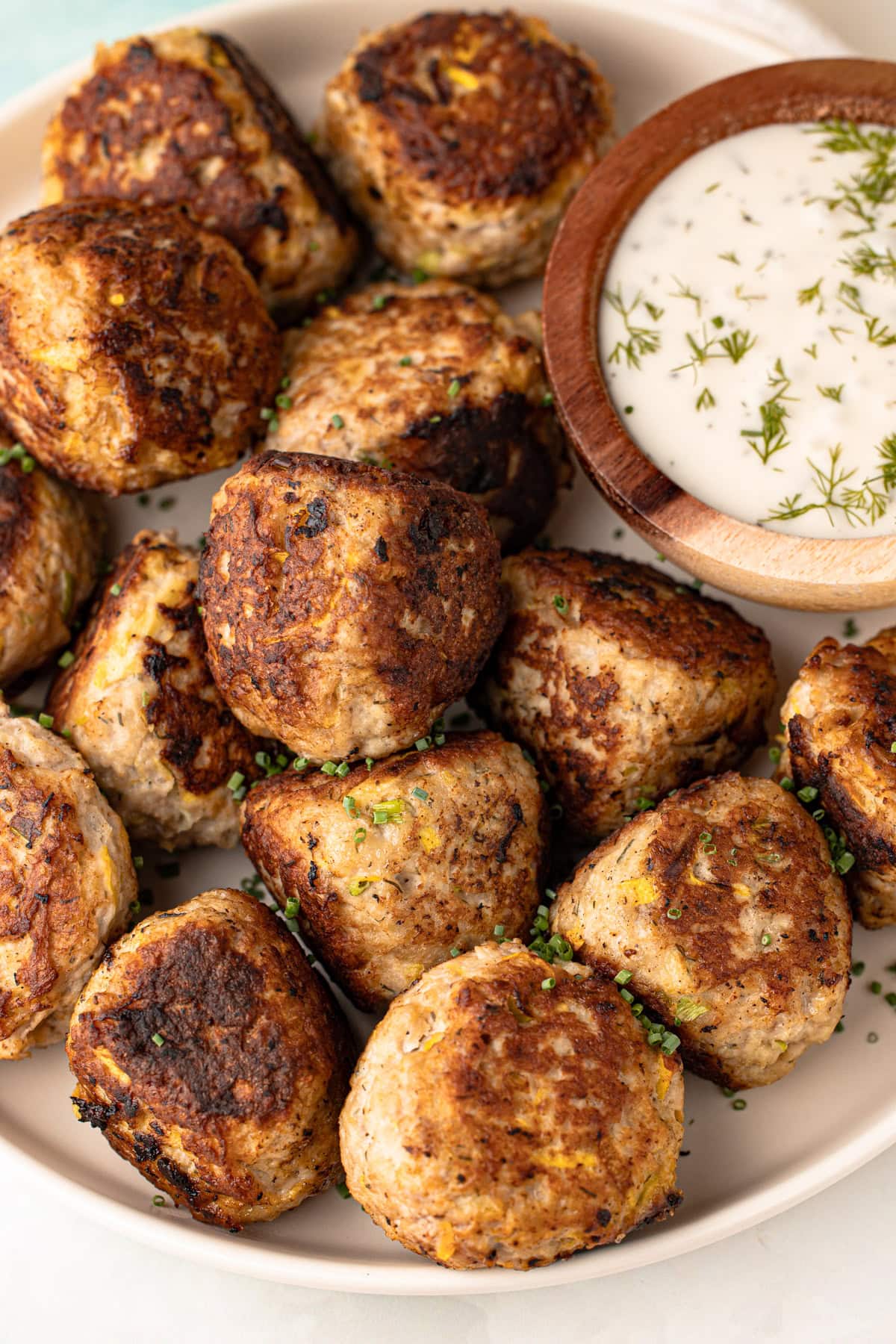 A serving platter of turkey zucchini meatballs with a creamy dipping sauce.