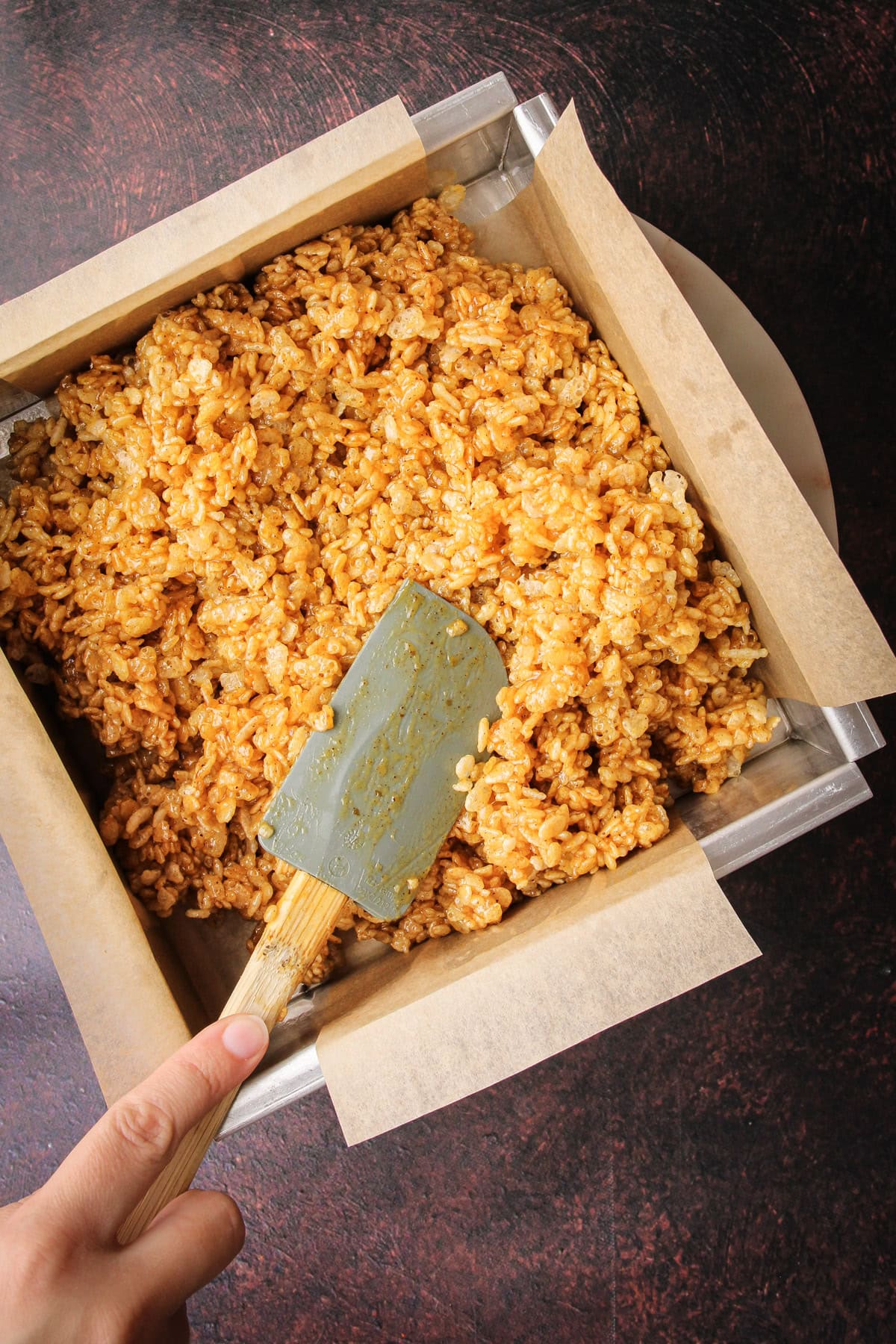Pushing rice crispy treats made with pumpkin into a baking dish.