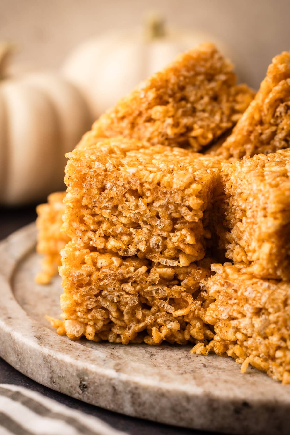 A batch of pumpkin rice crispy treats slice and served on a platter.