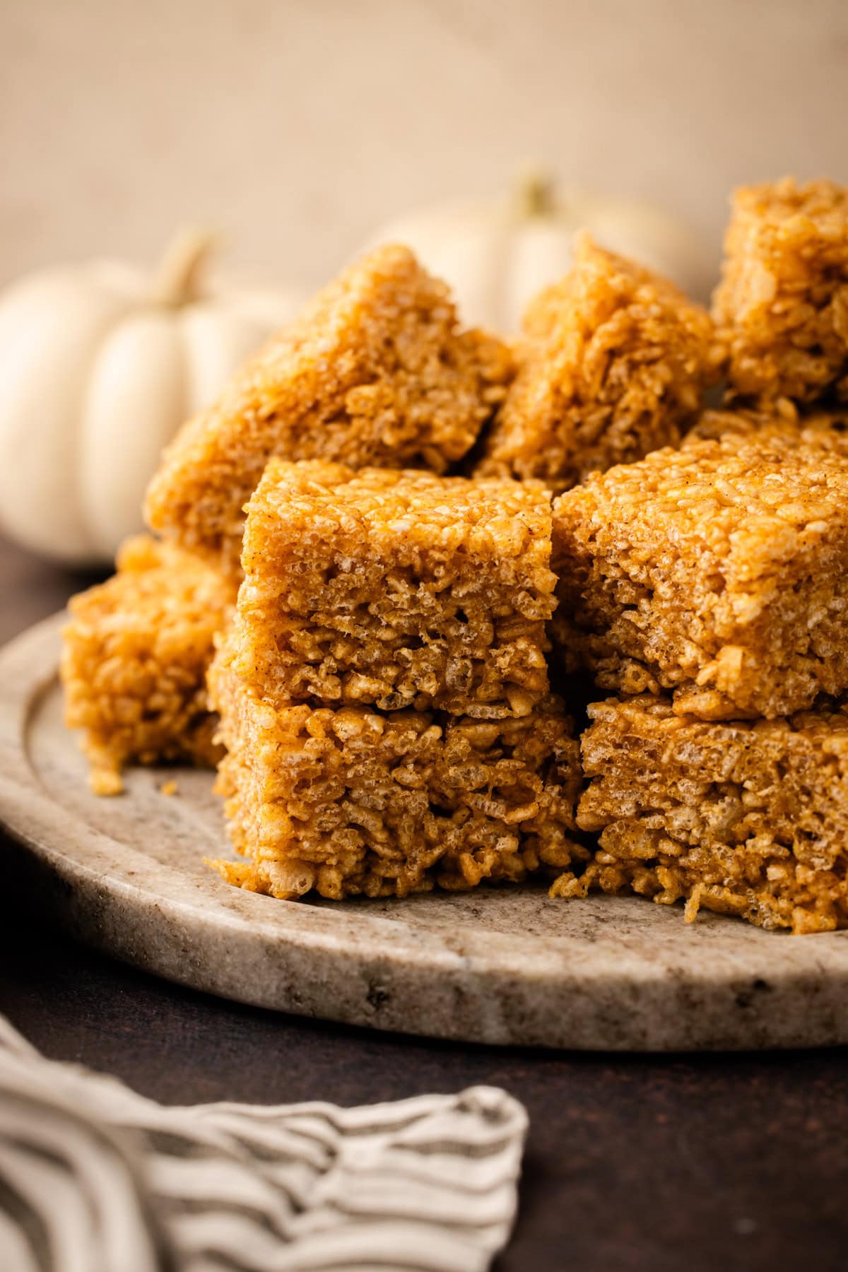 A batch of pumpkin rice crispy treats slice and served on a platter.