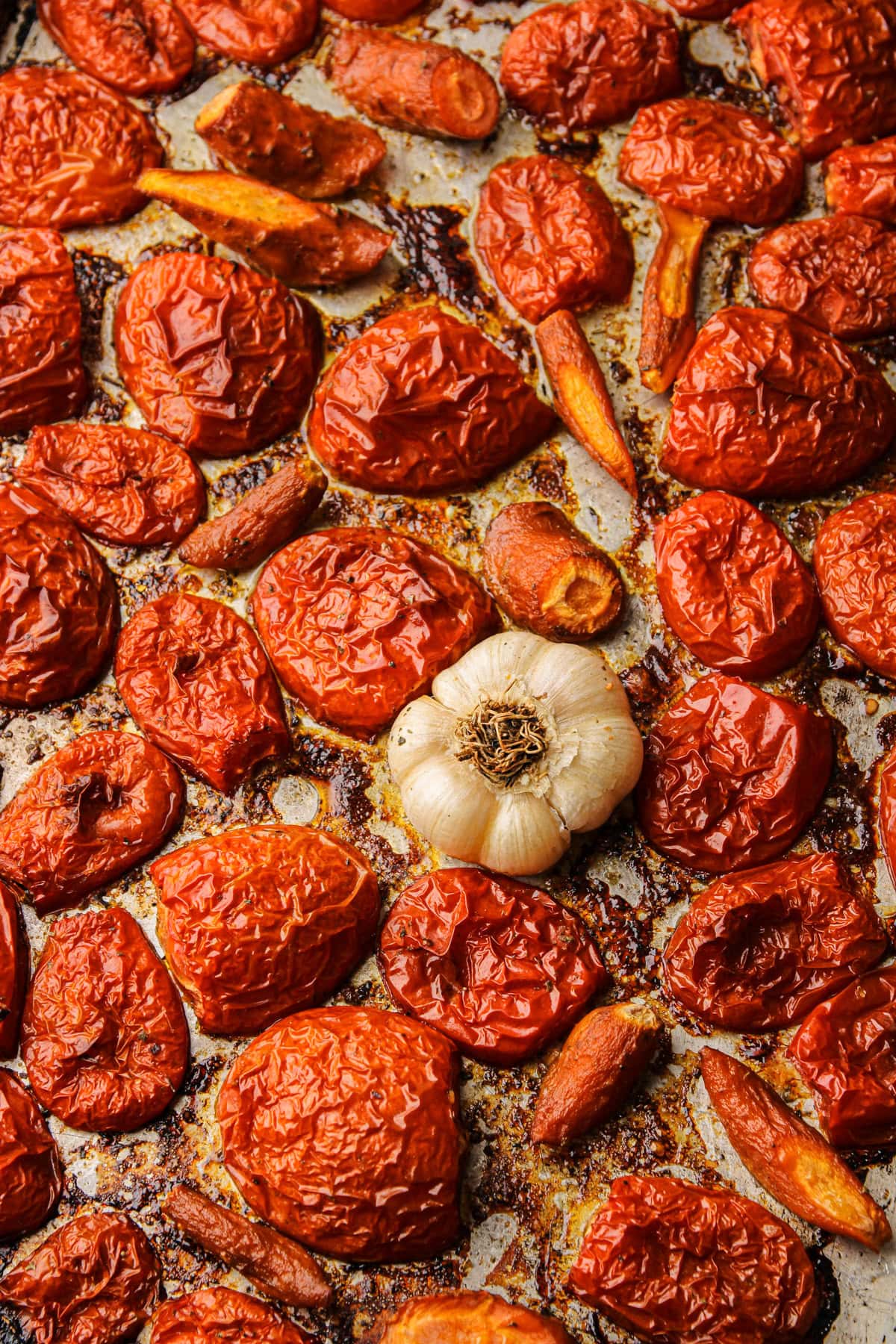 A sheet pan of roasted tomatoes and a head of garlic.